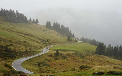 Route de montagne en lacets serpentant à travers des vallées alpines verdoyantes et boisées