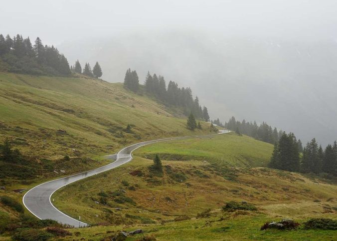 Route de montagne en lacets serpentant à travers des vallées alpines verdoyantes et boisées