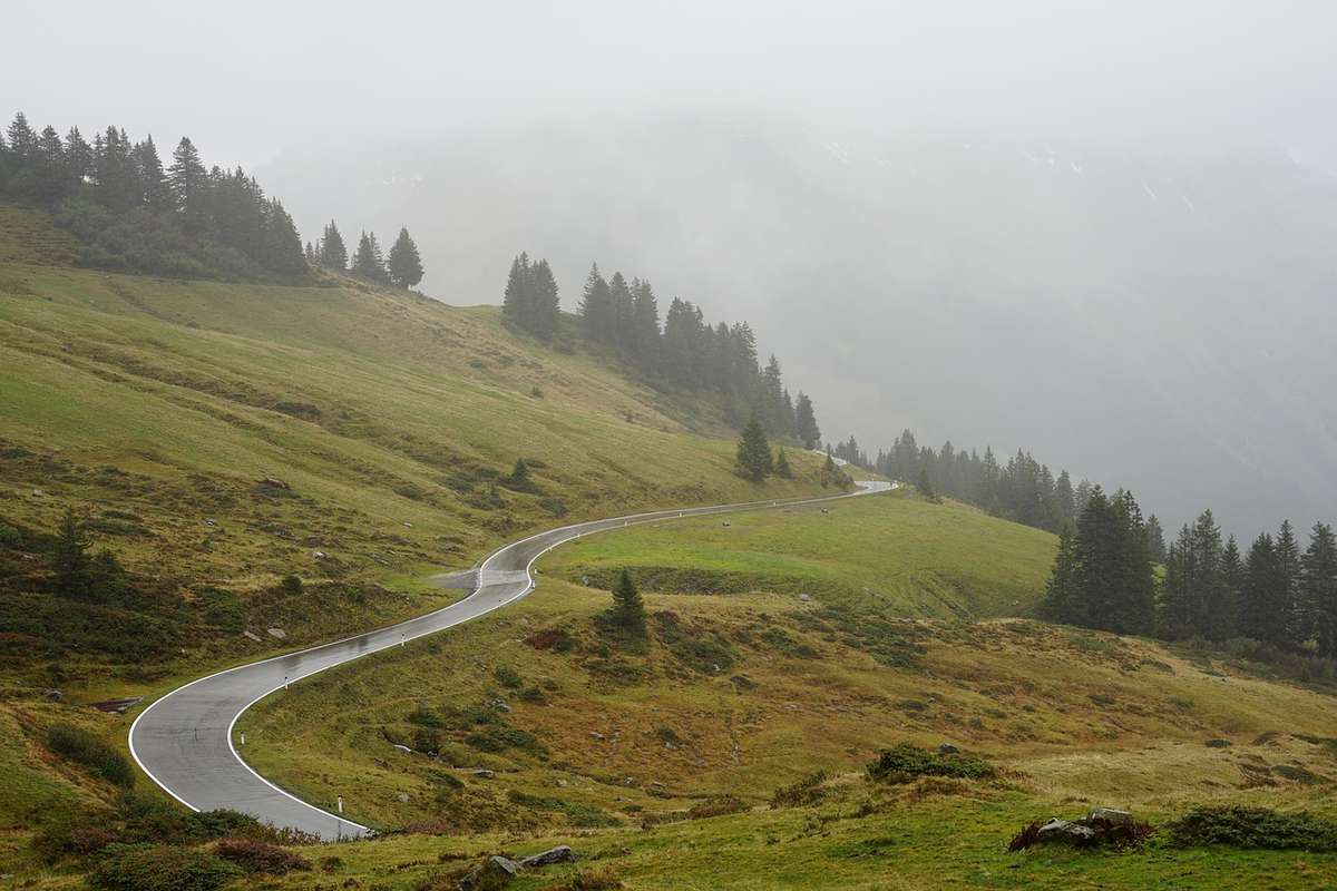 Route de montagne en lacets serpentant à travers des vallées alpines verdoyantes et boisées