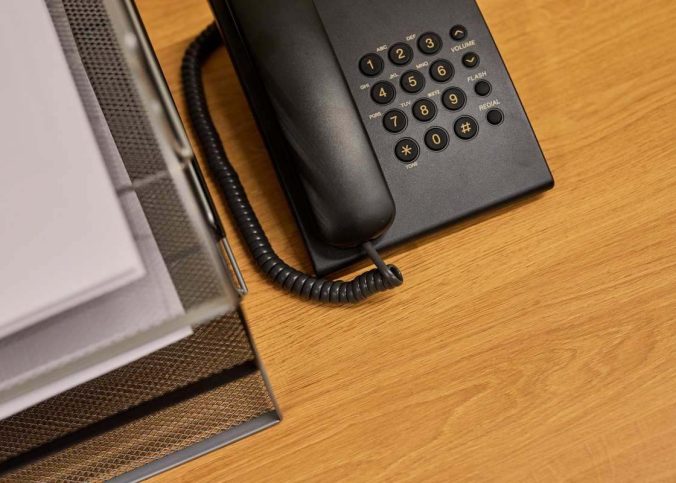 Un téléphone fixe posé sur un bureau en bois à côté d'un classeur