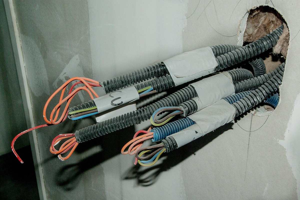Câbles électriques sortant d'un trou dans un mur, avec des fils orange et bleu Câbles électriques sortant d'un trou dans un mur, avec des fils orange et bleu